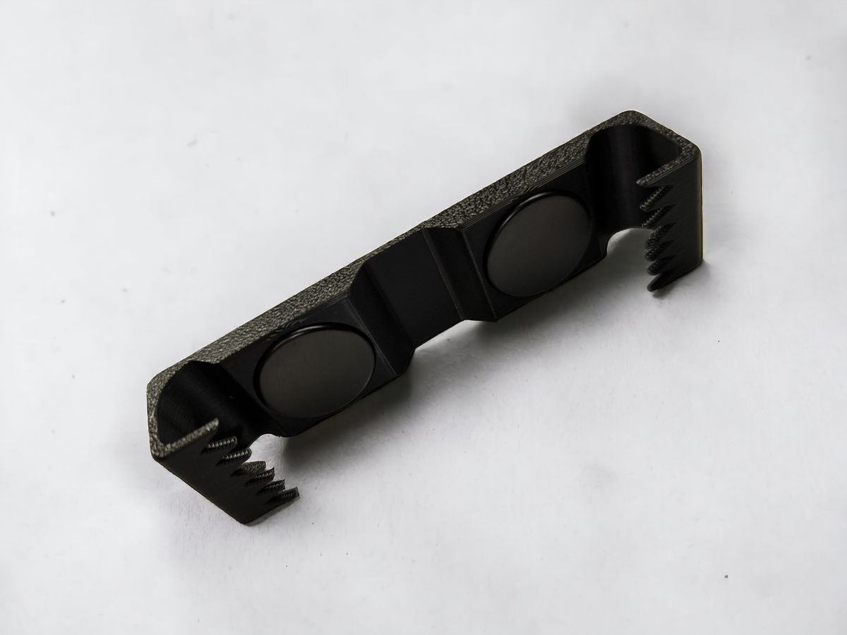 Schwarzer Aquakallax Magnethalter für HMF-Schwammfilter mit zwei runden Magneten und gezahnten seitlichen Halteklammern auf weißem Hintergrund.
