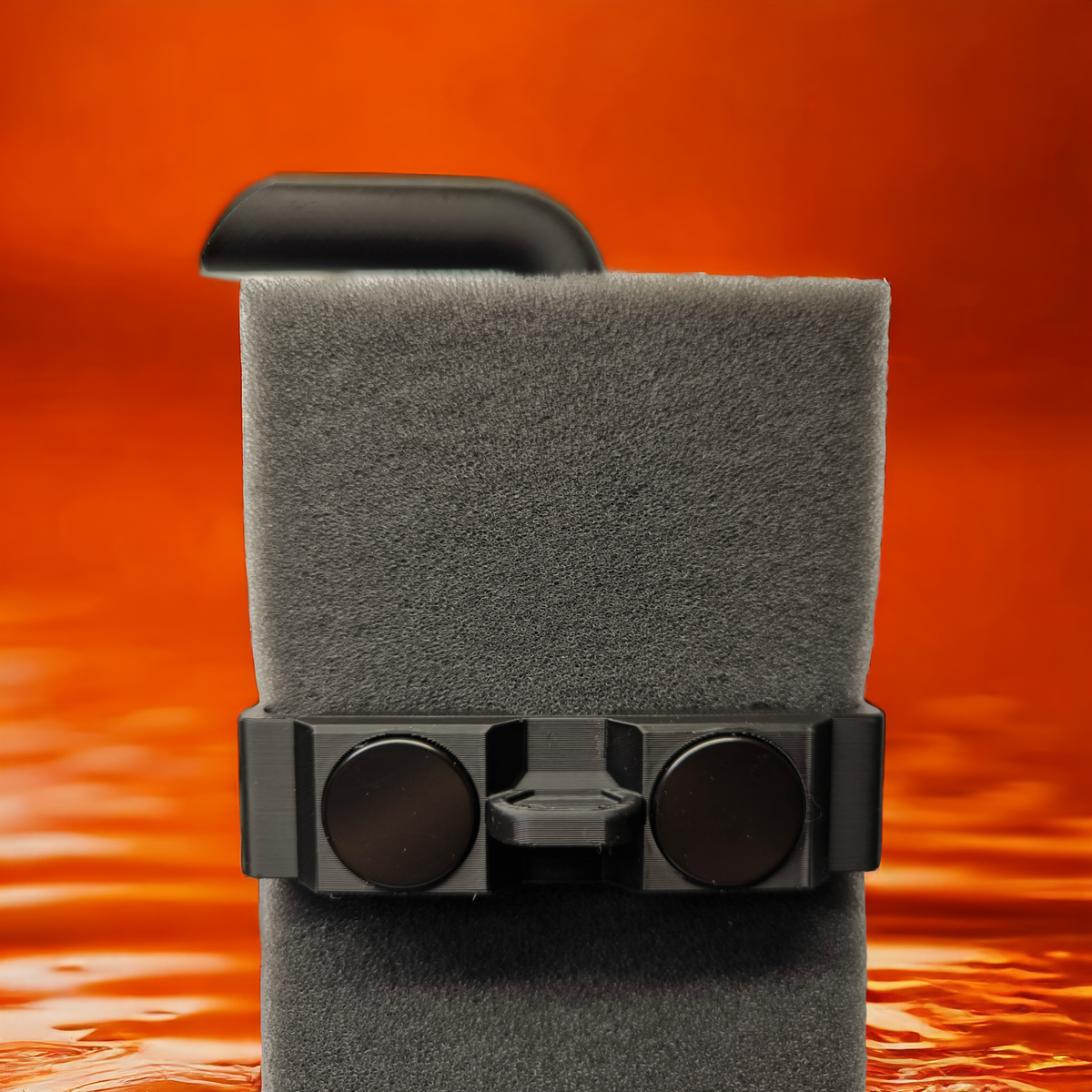 Aquakallax HMF-Schwammfilter mit schwarzem Halter und zwei runden Magneten vor orangefarbenem Wasserhintergrund.
