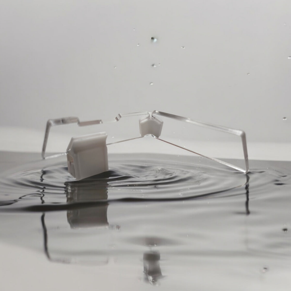Transparente Aquakallax JumpStop Sprungschutzecken mit weißen Klemmhaltern in flacher Seitenansicht vor Wasserhintergrund
