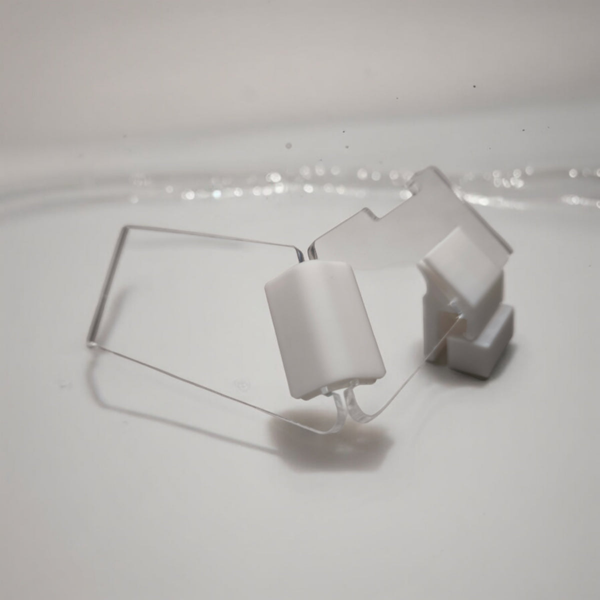 Zwei transparente Aquakallax JumpStop Sprungschutzecken mit weißen Klemmhaltern in schräger Ansicht