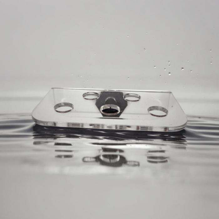 Transparenter Aquakallax ReefDeck für fünf Korallenplugs in der Frontansicht mit runden Öffnungen und schwarzem Magnethalter auf Wasserhintergrund
