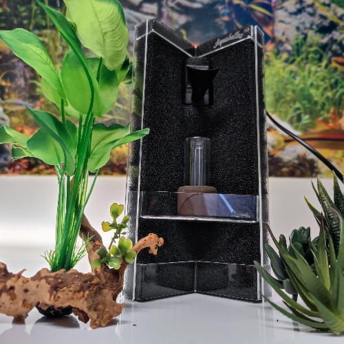 Aquakallax Konkav Mattenfilter mit transparenter Pflanzterrasse und integriertem Pumpenauslauf, Vorderansicht zwischen Pflanzen und einer Wurzel.