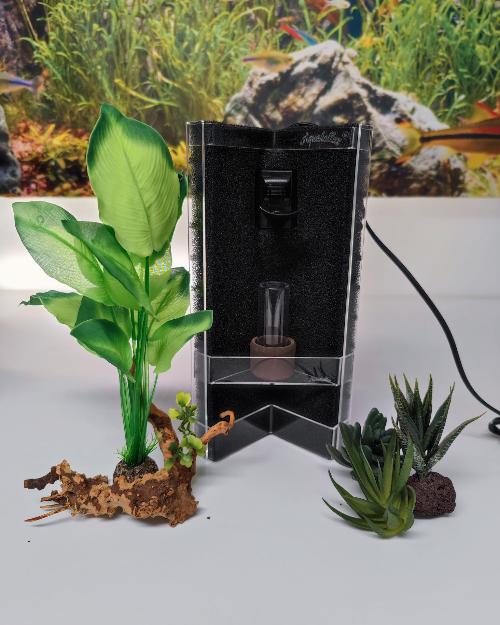 Aquakallax Konkav Mattenfilter mit schwarzem Pumpenauslauf und transparenter Pflanzterrasse, Gesamtansicht zwischen grünen Pflanzen und Wurzelholz.